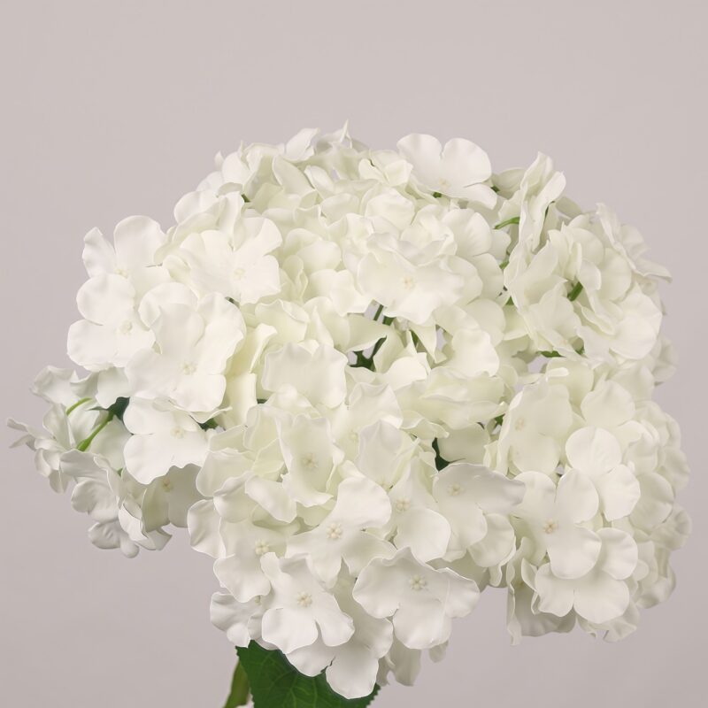 White faux hydrangea stem with full clustered blooms and realistic green leaves for wedding decor and event floral arrangements