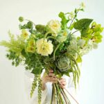 A lush green and yellow floral arrangement with artichoke and orchids
