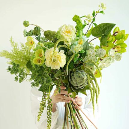 A lush green and yellow floral arrangement with artichoke and orchids