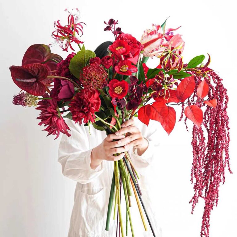 Large red flower bundle with deep red and crimson blooms held by a person in a white shirt.