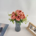 Artificial silk rose bouquet featuring seven coral blooms arranged in a modern gray vase.
