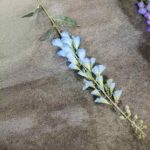 Fake silk bluebell flower stem arrangement lying on light beige sand.