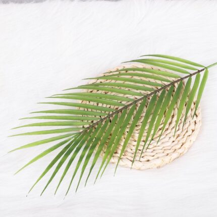 Artificial green palm leaf resting on a woven straw decorative basket accent.