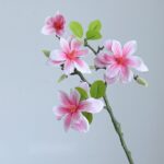 Artificial pink silk magnolia floral arrangement branch decor with realistic green foliage.