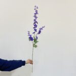 Silk delphinium stems in deep purple colors, bundled and displayed against a white background.