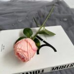 Artificial pink silk rose with green stem displayed on white gift box packaging.