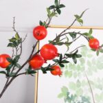 Faux pomegranate branches with lush green leaves, perfect for seasonal home decor and centerpieces.
