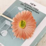 Pink gerbera daisy flower craft decoration on stick, styled on a book about Scandinavian design.