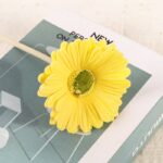 Artificial yellow gerbera daisy craft flower accessory displayed on a promotional booklet.