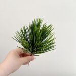 Hand holding realistic faux green palm leaves perfect for wedding decor or home use.