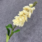 Artificial pale yellow flower spray with green leaves on a grey background