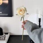 Elegant cream faux silk rose held in a hand, perfect artificial floral decor and everlasting bouquet for home use.