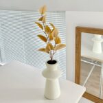 Vase displaying artificial gold silk leaves decor on a modern white tabletop surface.