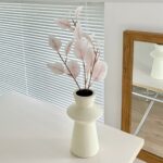 Faux pink eucalyptus branch arrangement displayed in a minimalist white ceramic vase.