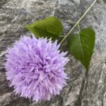 Purple silk pompon ball bouquet centerpiece with green faux flower stems on stone