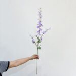 Holding artificial purple silk delphinium flowers bouquet for home decor use