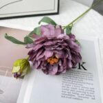 Two heads of realistic artificial silk peonies in deep purple tones with greenery.