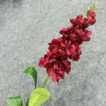 Close-up of a deep red artificial flower spray with green leaves on a gray background.