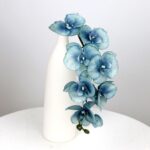 Elegant faux blue orchid arrangement of 8 heads displayed in a minimalist white ceramic vase.