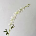 White artificial silk Delphinium floral stem arrangement on a plant background.