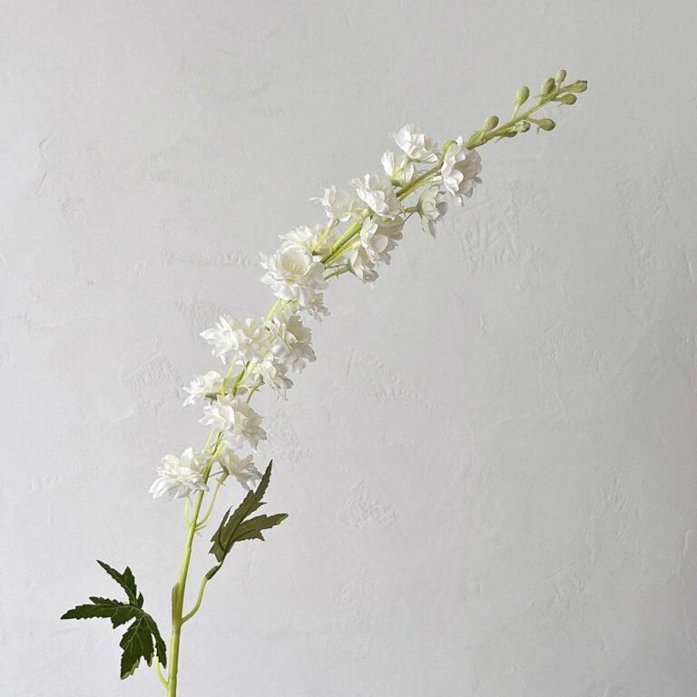White artificial silk Delphinium floral stem arrangement on a plant background.