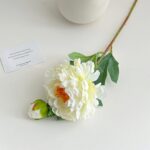 Two heads of artificial cream peony flowers displayed on white surface with a loving message card.