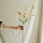 Hand displaying a delicate silk vintage daisy arrangement with warm orange blossoms.