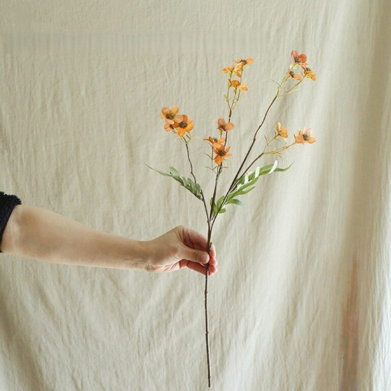 Hand displaying a delicate silk vintage daisy arrangement with warm orange blossoms.