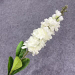 Artificial white flower spray with green leaves on a grey background