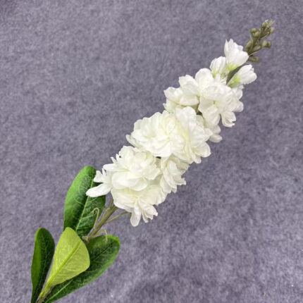 Artificial white flower spray with green leaves on a grey background