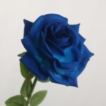 Single stem artificial royal blue rose flower with green leaves on a light neutral background