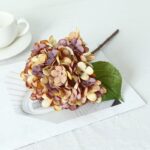 Silk artificial hydrangea blossom arrangement next to a cup of tea set