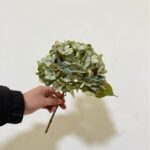 Hand holding realistic silk hydrangea flower bouquet for artificial home decor.