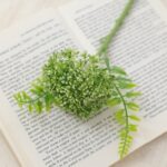 Realistic artificial flower arrangement placed on an open book next to foliage.