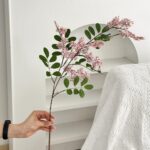 Hand displaying a branch of artificial flower blooms and leaves, perfect for indoor decor.