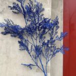 Blue artificial flower arrangement mounted on a wall, featuring realistic silk flower branches.