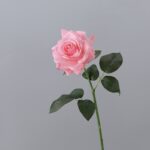 Realistic artificial flower pink rose bloom on stem with green leaves