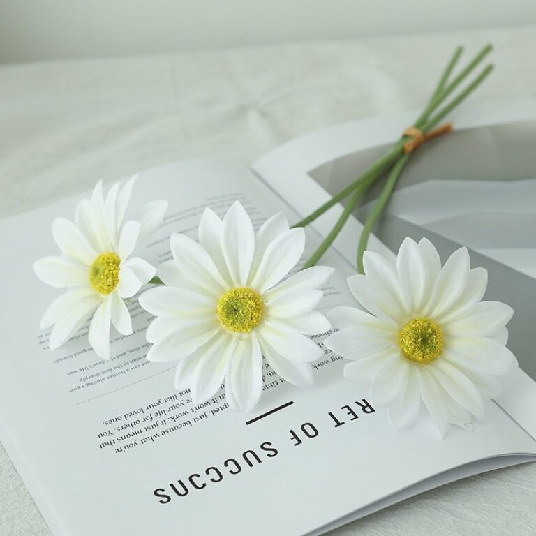 White artificial silk flower arrangement with stems displayed on an open book.