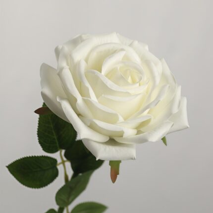 Single stem artificial white rose flower with green leaves on a light neutral background