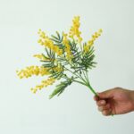 Artificial yellow acacia flower cluster bouquet with green foliage.