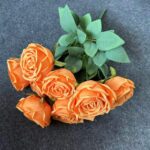 Bunch of seven artificial orange silk roses with green foliage.