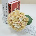 Realistic silk hydrangea bloom artificial flower arrangement next to books.
