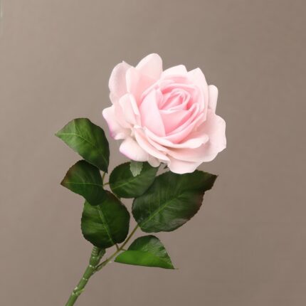 Single soft pink artificial rose stem with full-bloomed petals and rich green leaves against a neutral beige background.