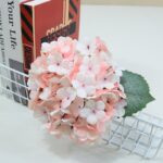 Elegant blush pink silk hydrangea bouquet displayed on a white surface next to design books.