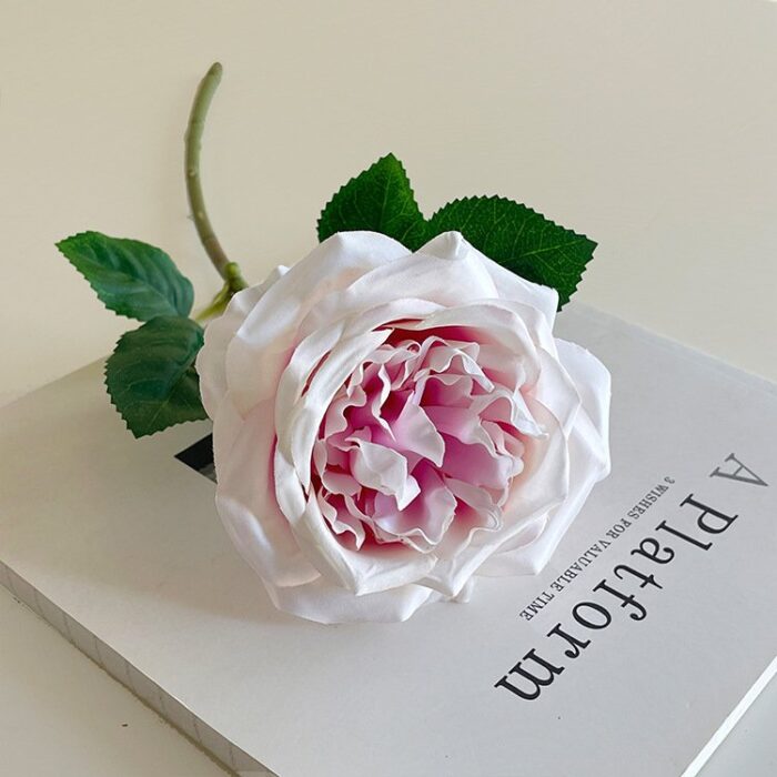 Realistic pink artificial rose resting on a book, perfect as faux wedding flowers.