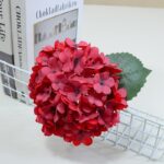 Red silk hydrangea artificial flower arrangement displayed near books.