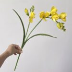 Hand holding vibrant yellow faux Freesia bouquet, perfect artificial flower decoration.
