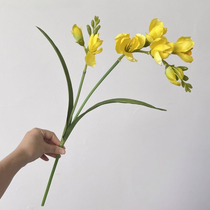 Hand holding vibrant yellow faux Freesia bouquet, perfect artificial flower decoration.