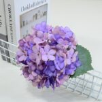 Realistic faux purple silk hydrangea arrangement displayed next to a book.
